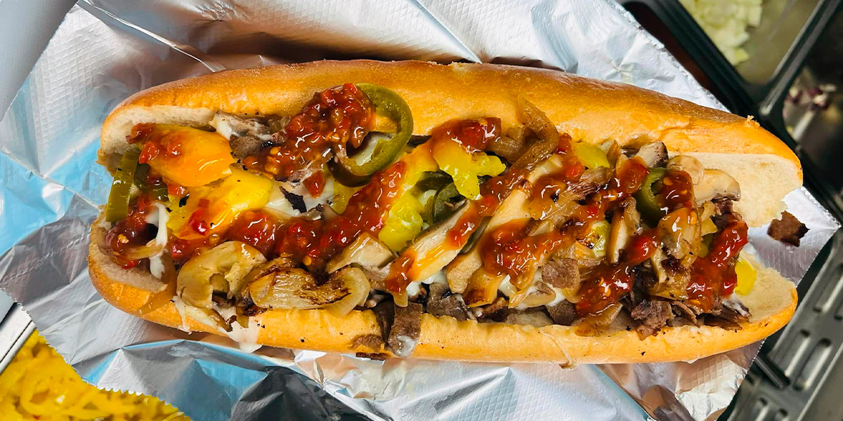 An image of a cheesesteak loaded with peppers, cheese, and sauce from Eddies Famous Cheesesteaks and Grille in downtown Akron.