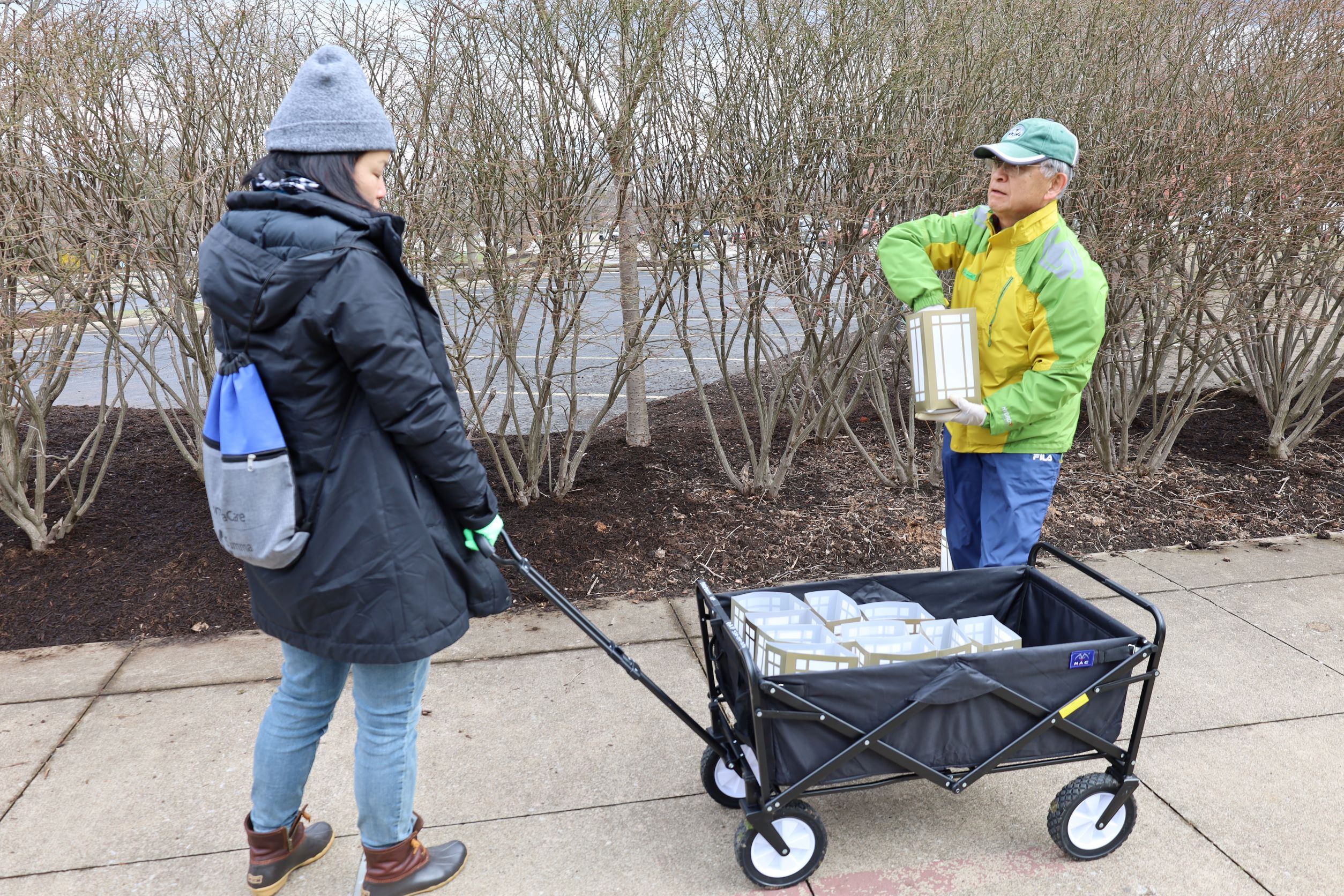 Two volunteers in coats and hats pulling a wagon full of luminaries along a concrete path
