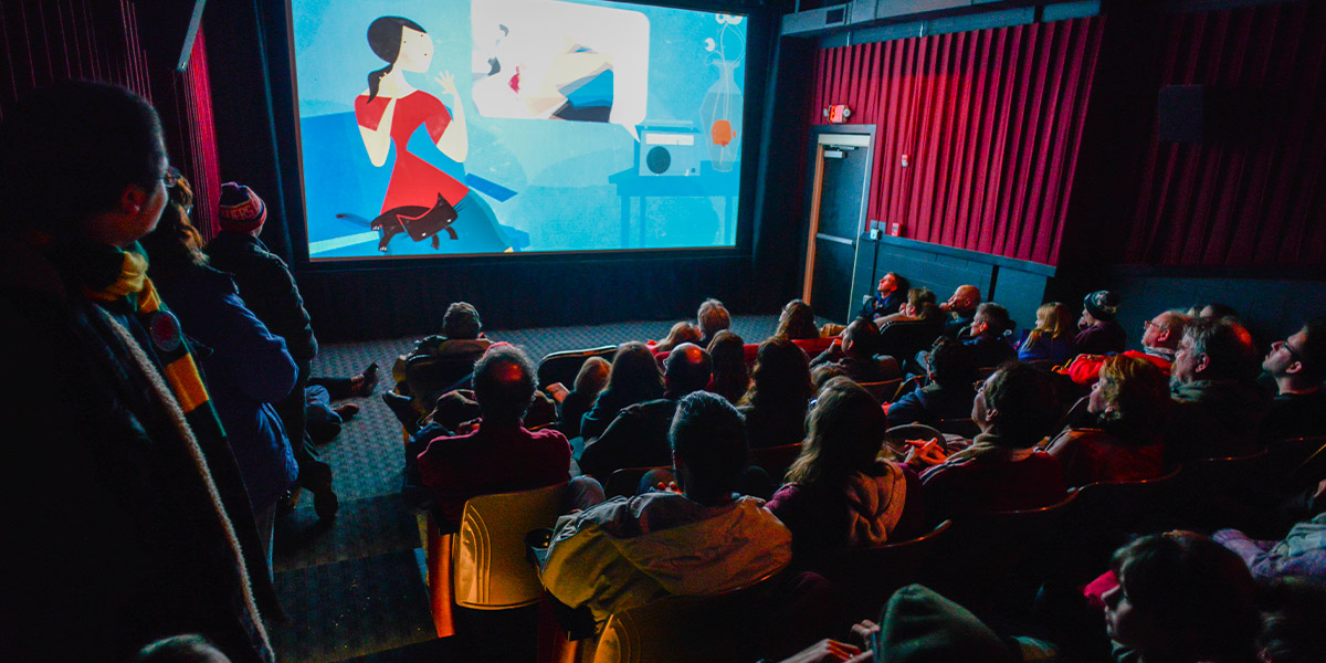 An image of a crowed movie theatre with a movie playing on screen.